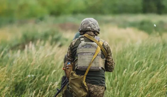 Вакансія Розвідник у Збройних Силах України: військовий у камуфляжі йде через високу траву у польових умовах, демонструючи витривалість, професіоналізм і готовність до виконання бойових завдань.