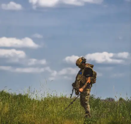 Вакансія Сапер у Збройних Силах України: військовий у камуфляжі з металошукачем досліджує поле, демонструючи уважність, професіоналізм і підготовку до виконання складних завдань.